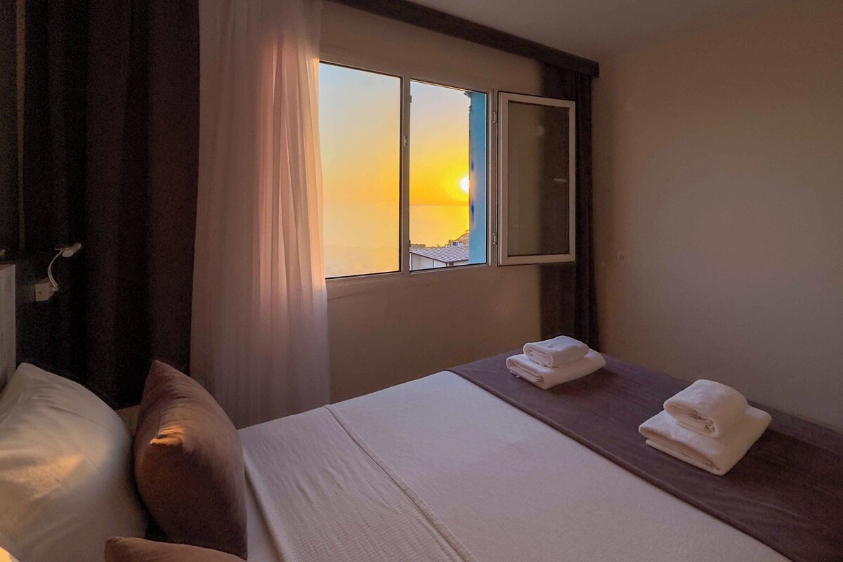 A hotel room with a bed, a nightstand, a window with curtains, and a mirror.
