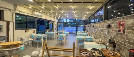 A restaurant with tables and chairs, a brick wall with posters, and a view through large windows.