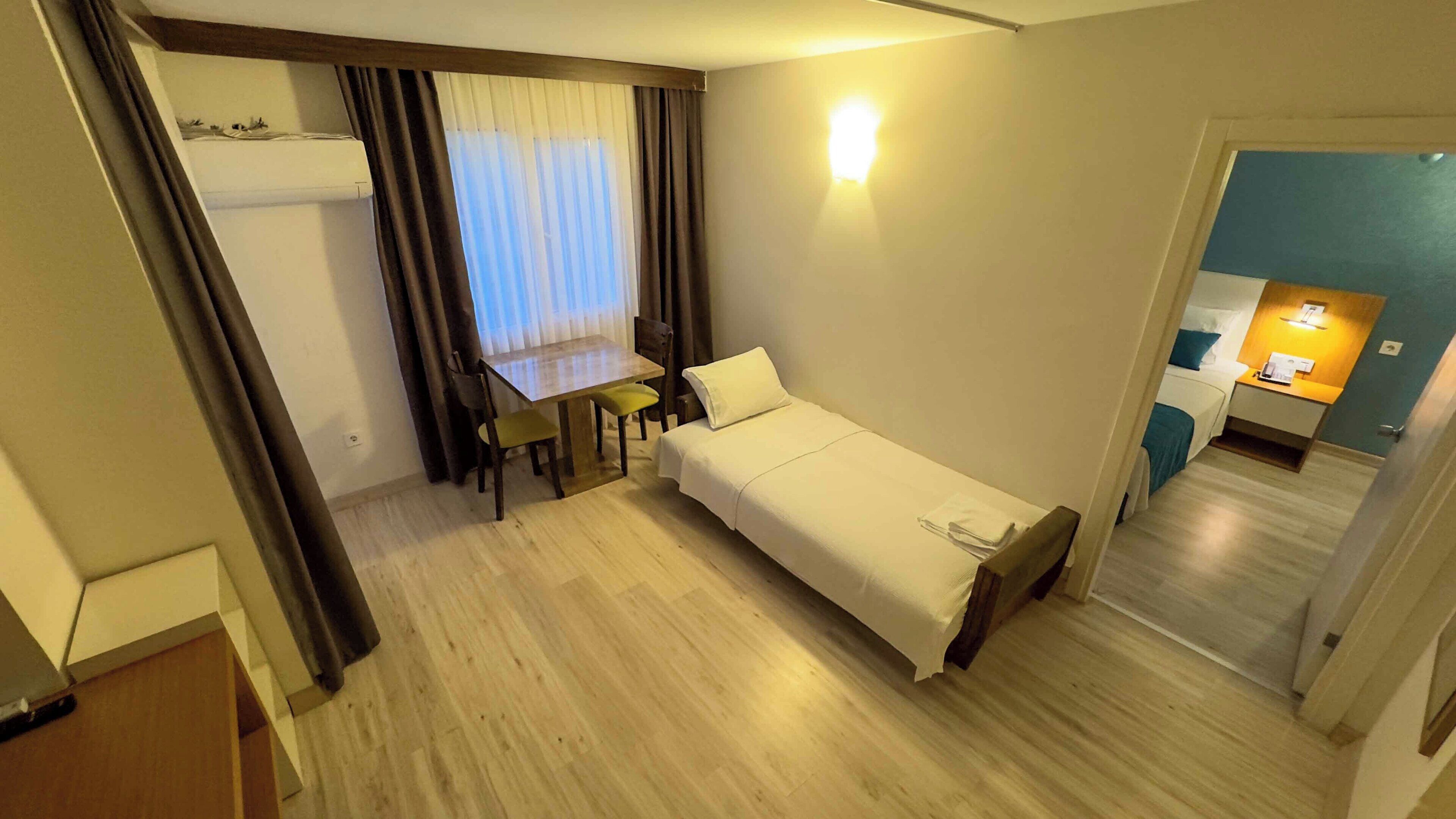 A compact hotel room with a single bed, a small dining table, and a separate kitchenette area.