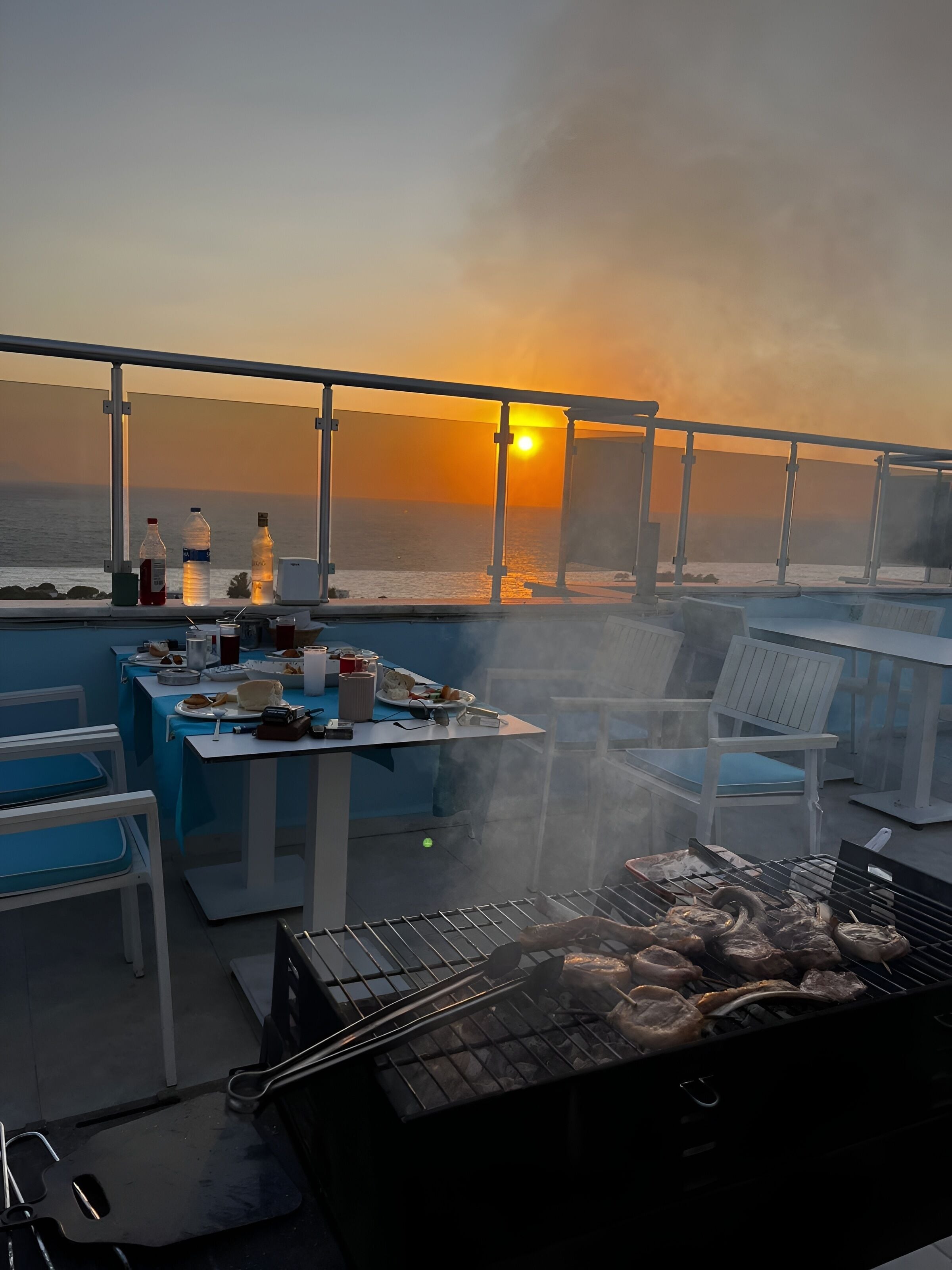 Un bar situé sur le toit, avec un barbecue, une table à manger, des chaises et des bouteilles.