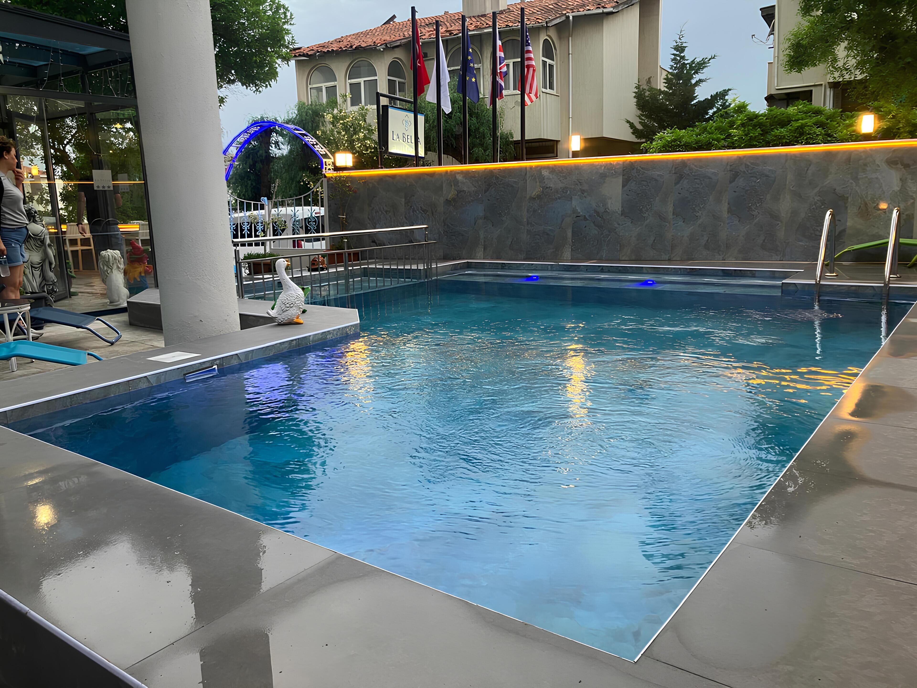 A swimming pool with a duck sculpture, flags, and a building in the background.