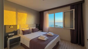 A hotel room with a bed, bedside table, phone, and a window with a view. - La Bella Suite Hotel (Kusadasi)