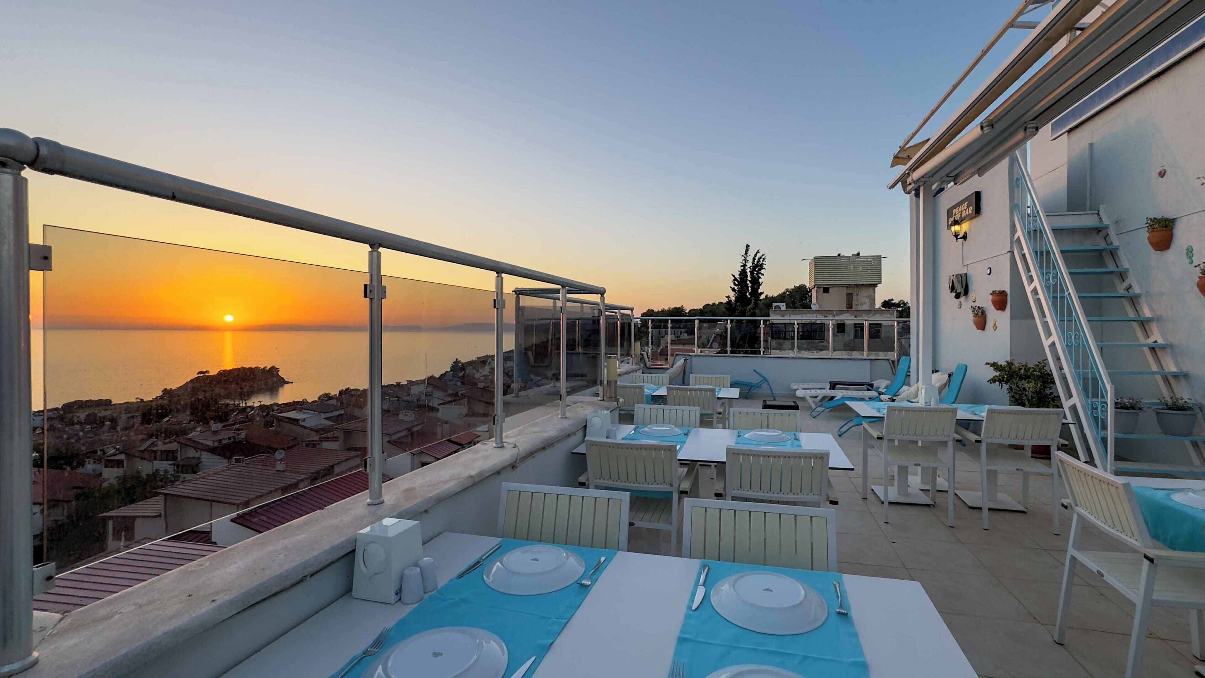 Terraza en la azotea con mesas dispuestas para comer, con vistas a un atardecer costero.