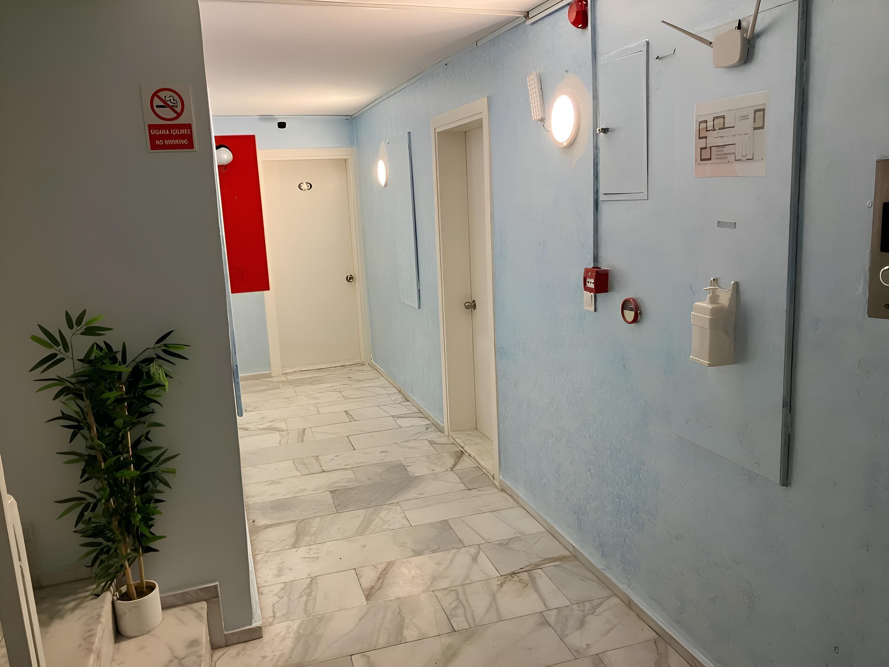 A hallway with a marble floor, a potted plant, a red sign, and a wall-mounted light fixture.