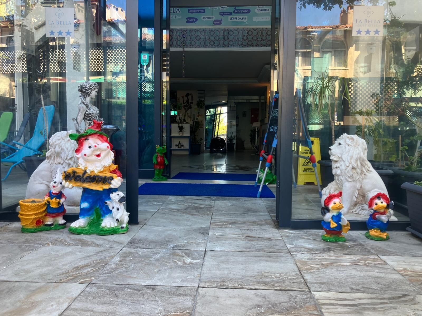 A hotel entrance with a welcome sign, a lion statue, and a dog statue.