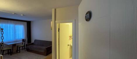 A living room with a sofa, a small table, and a chair. There is a door with a number sign on it.