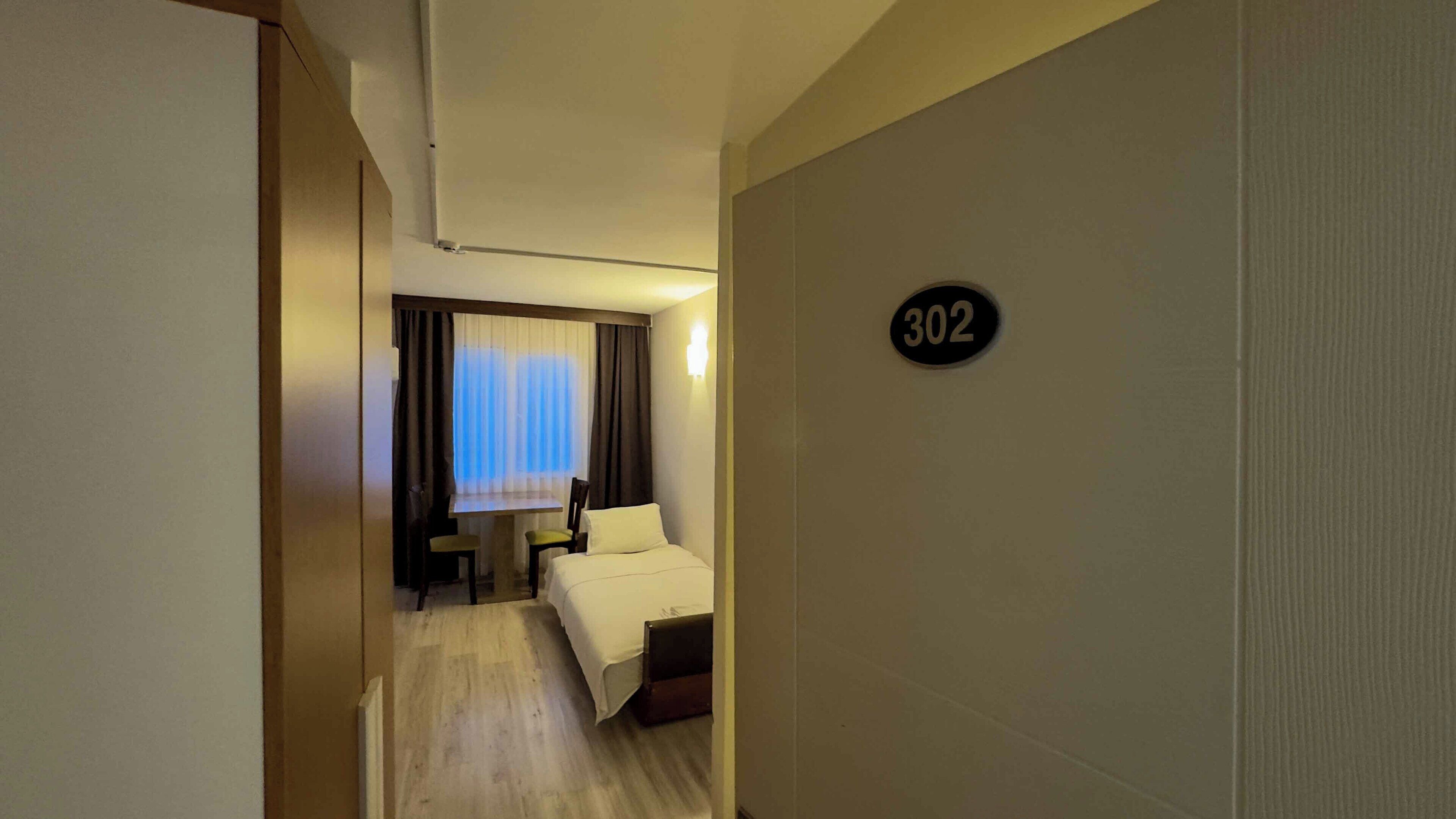 Habitación de hotel con una cama, un escritorio y una silla. La habitación tiene un cartel con un número en la pared.