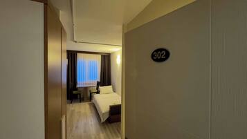 Habitación de hotel con una cama, un escritorio y una silla. La habitación tiene un cartel con un número en la pared.