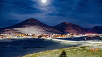 A nighttime landscape with a prominent mountain and a lit town in the foreground.
