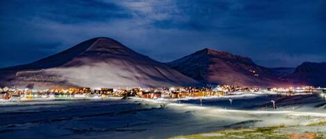 A nighttime landscape with a prominent mountain and a lit town in the foreground.