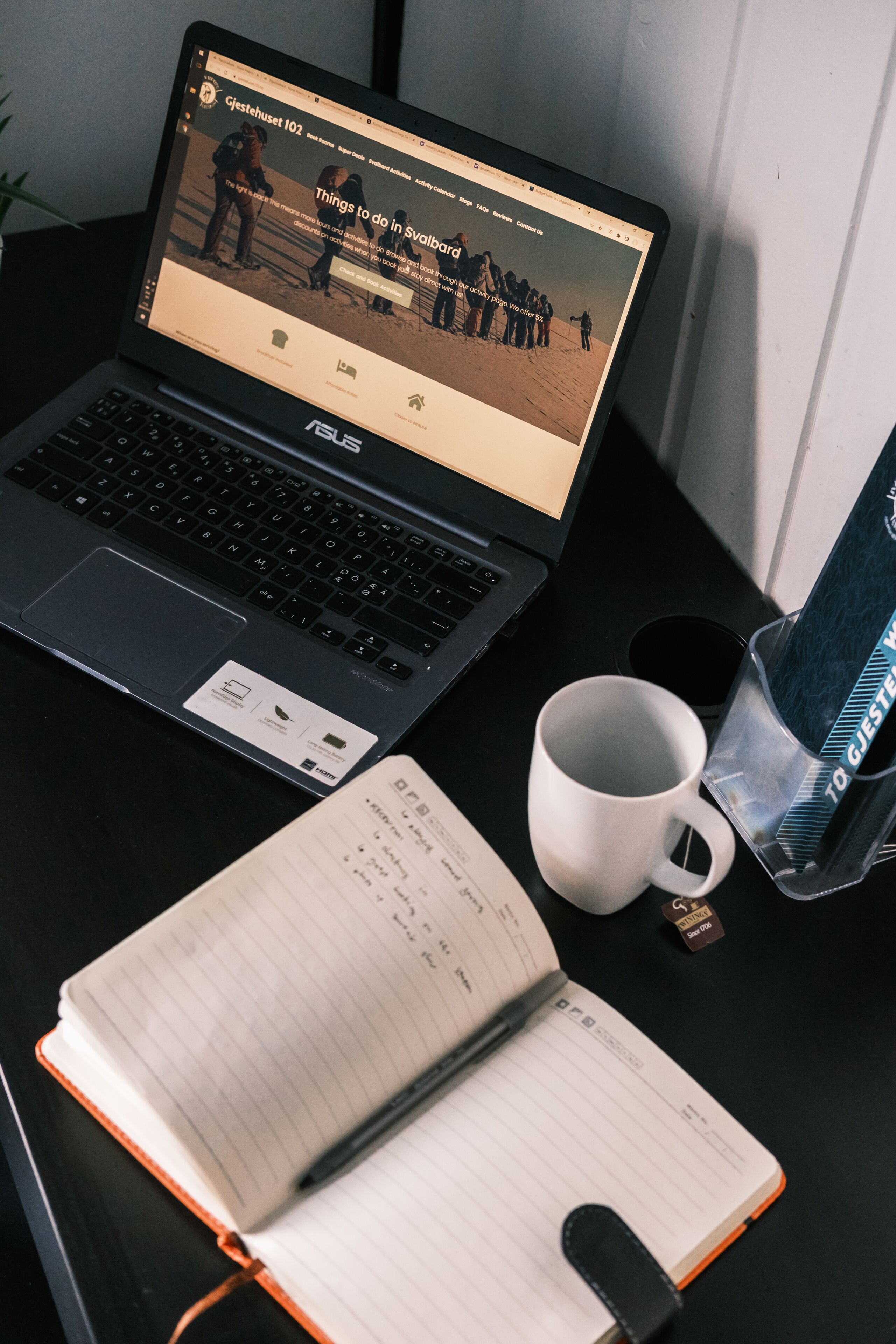 A laptop on a desk with a notebook, a pen, a mug, and a water bottle.