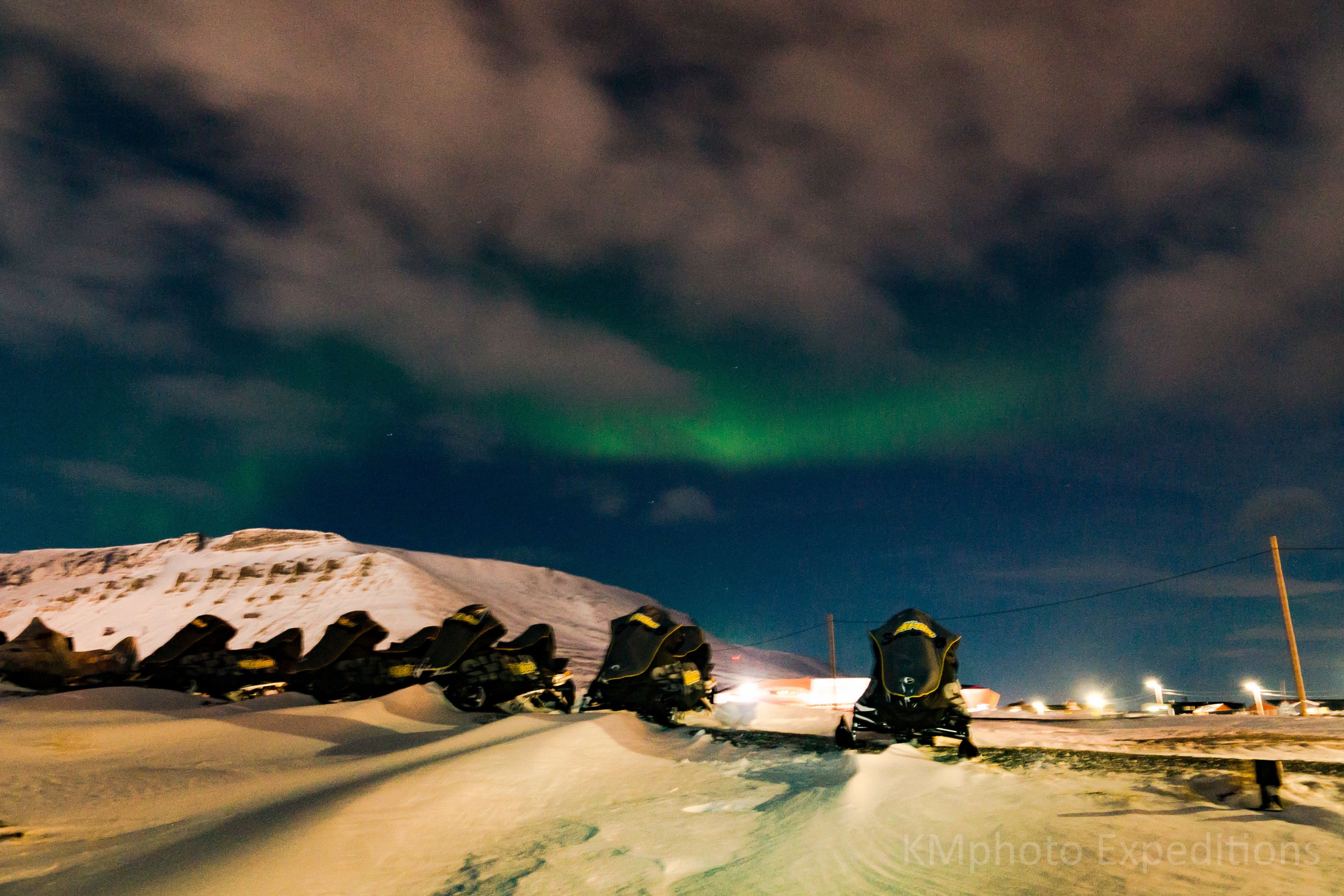 A row of snowmobiles parked on a snowy slope with a mountain in the background.