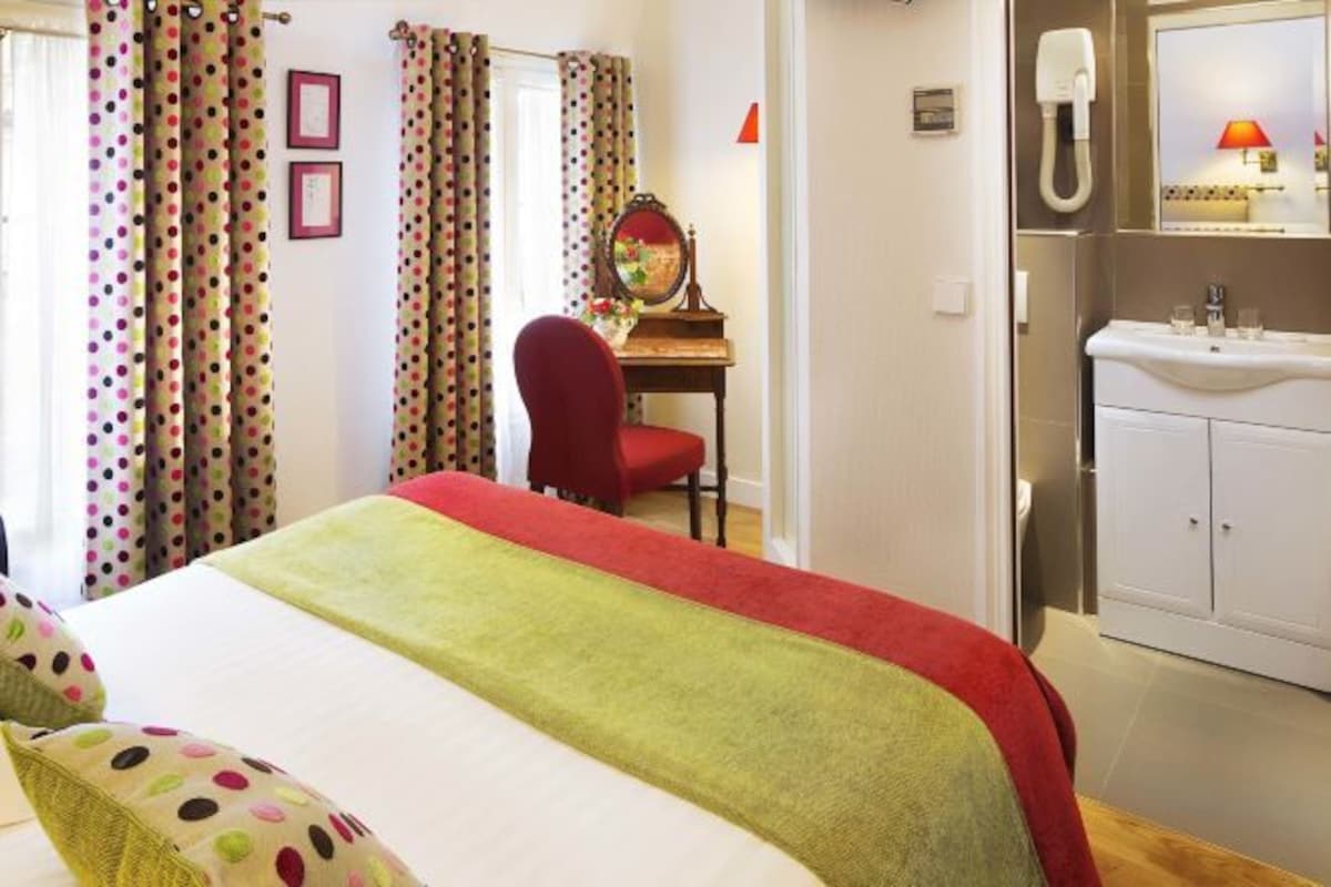 A hotel room with a bed, a desk, a chair, a mirror, a telephone, and a sink.