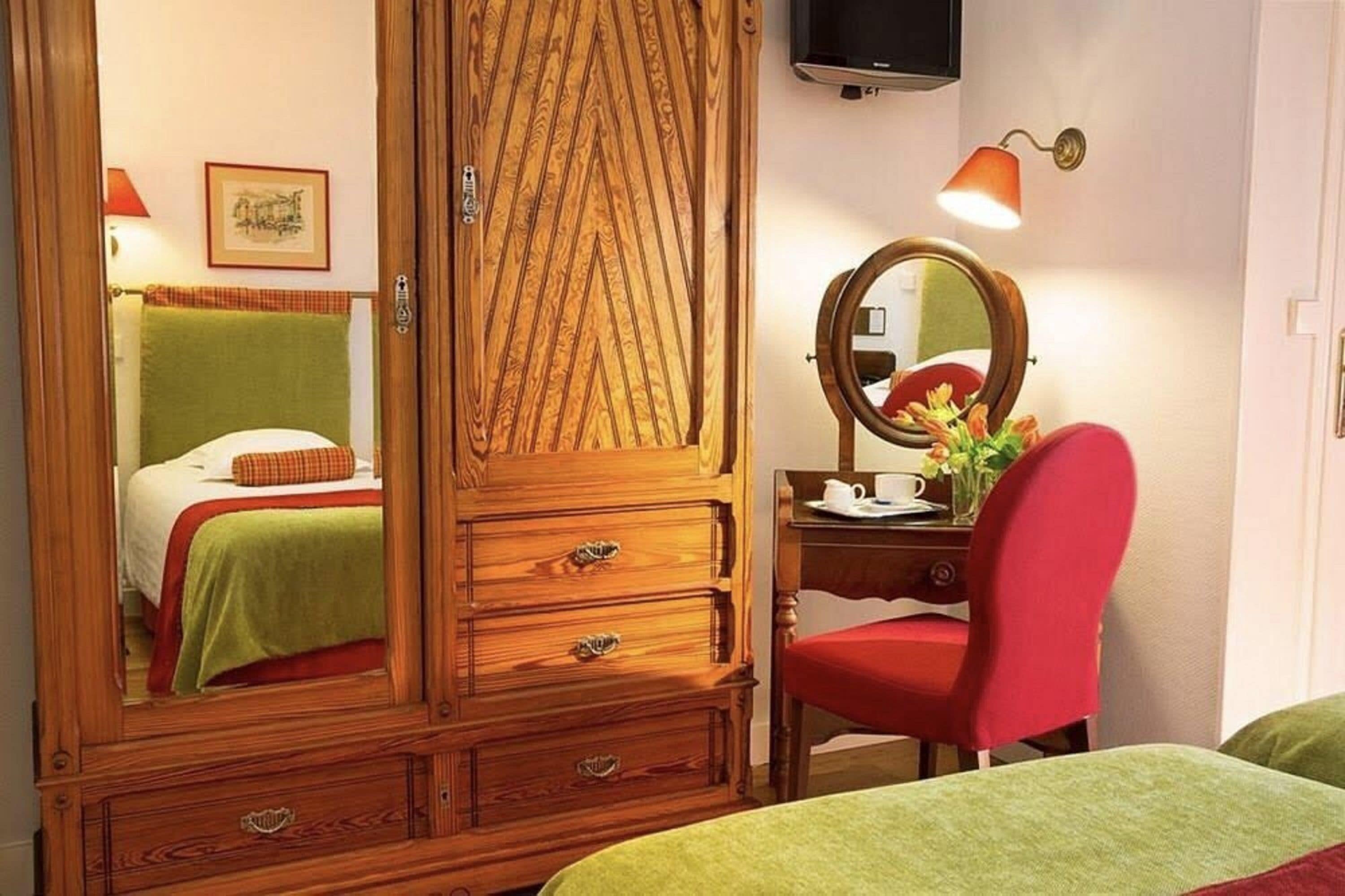 Une chambre à coucher avec une armoire en bois, une table de chevet avec un miroir, une chaise rouge et un lit avec une literie verte.