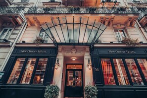 The facade of the New Orient Hotel with a classic architectural style, featuring a central entrance with a glass canopy and two symmetrical wings. - New Orient Hôtel (Paris)