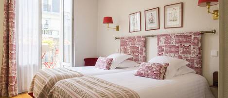 A hotel room with two beds, a window with curtains, and wall-mounted lamps.