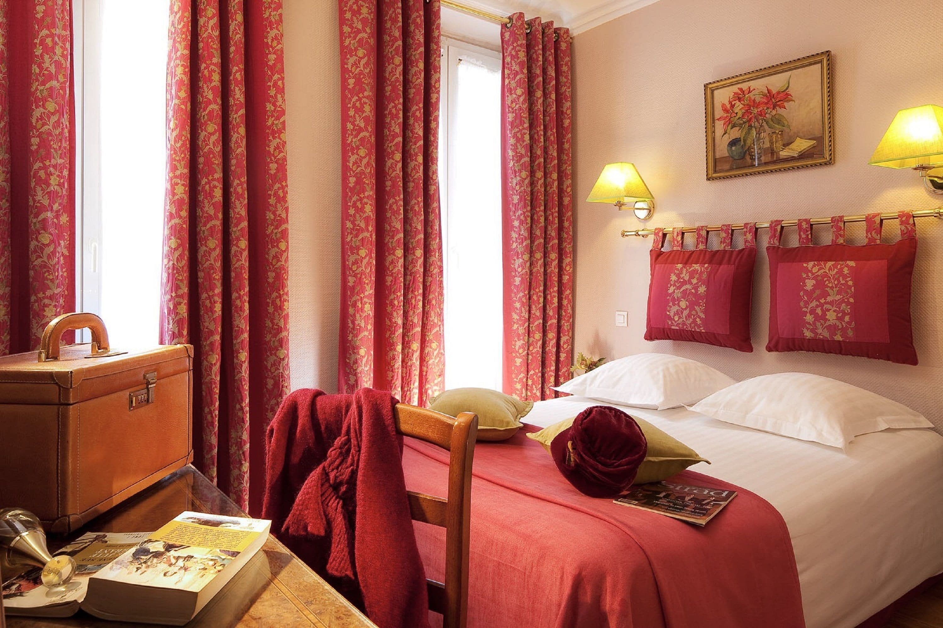 Una camera d'albergo con un letto, una scrivania con una valigia, una sedia e una lampada.