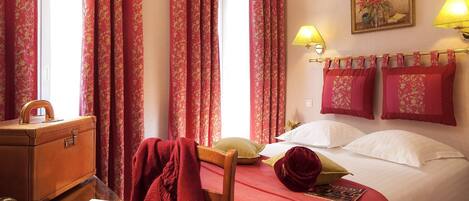 Una camera d'albergo con un letto, una scrivania con una valigia, una sedia e una lampada.