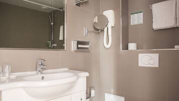 A modern bathroom with a large sink, mirror, towel rack, and a wall-mounted heater.
