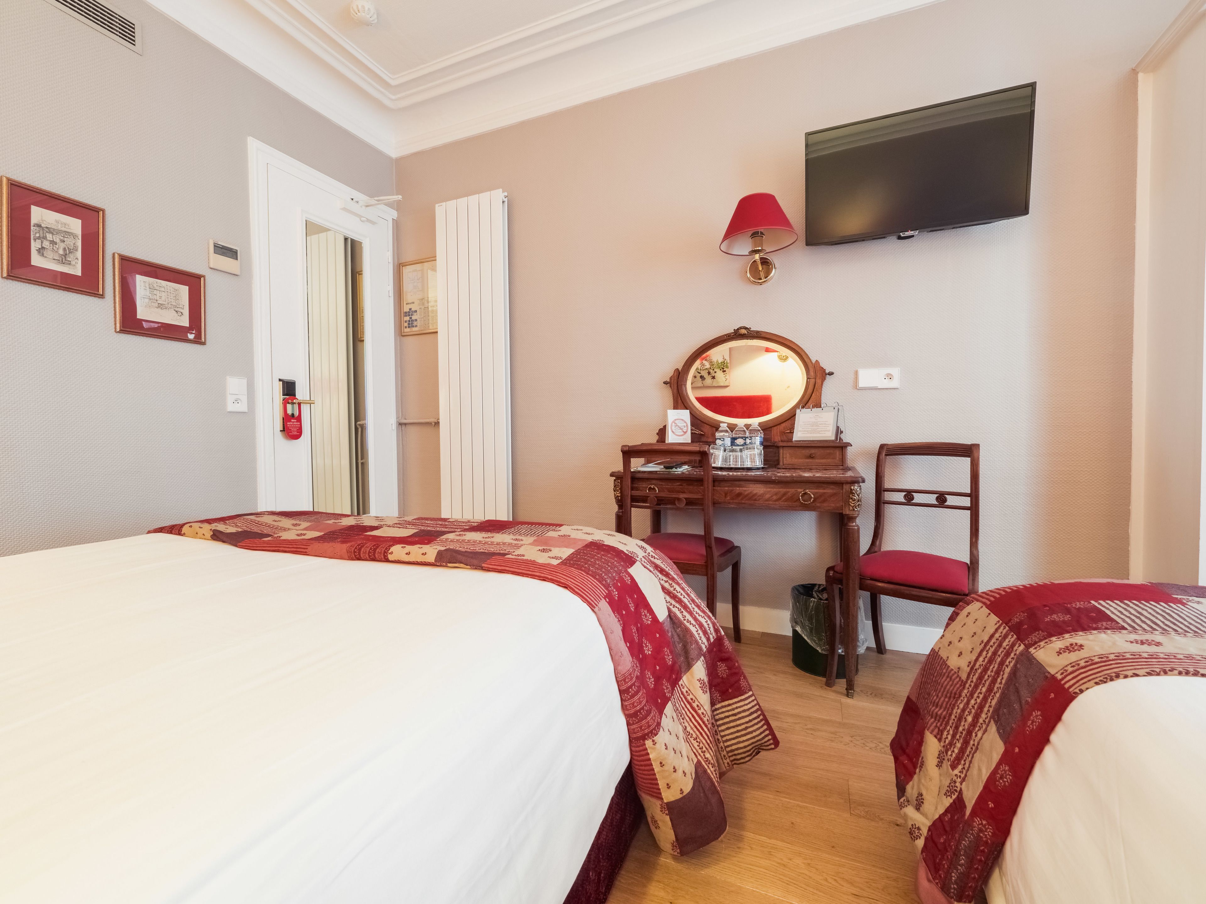 A hotel room with two beds, a desk with a mirror, a television, and framed pictures on the wall.