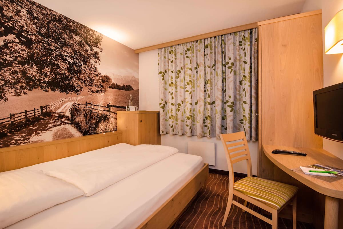 Ein Hotelzimmer mit einem Bett, einem Schreibtisch mit Stuhl, einem Fernseher und einem Wandgemälde.