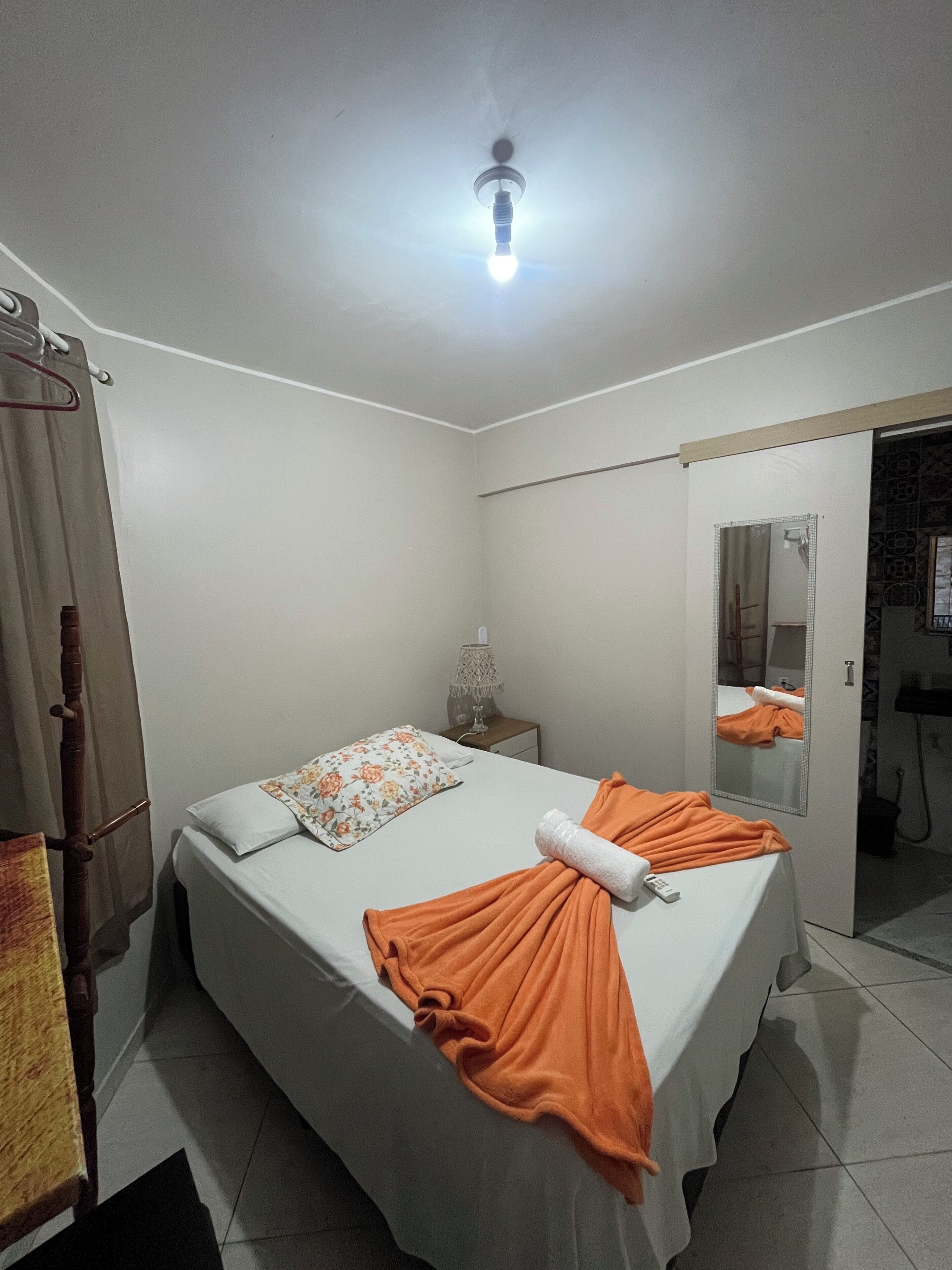 Habitación de hotel con cama, mesita de noche, espejo y perchero.