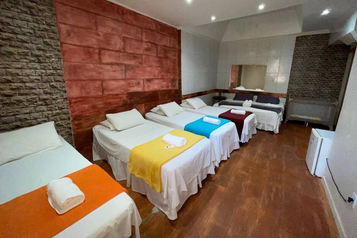 A hotel room with four beds arranged in a row, a stone wall on one side, and a red accent wall on the other.