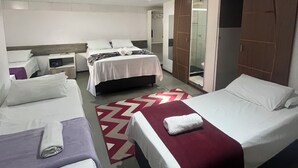 A hotel room with three beds, a red and white patterned rug, and a sliding door closet.