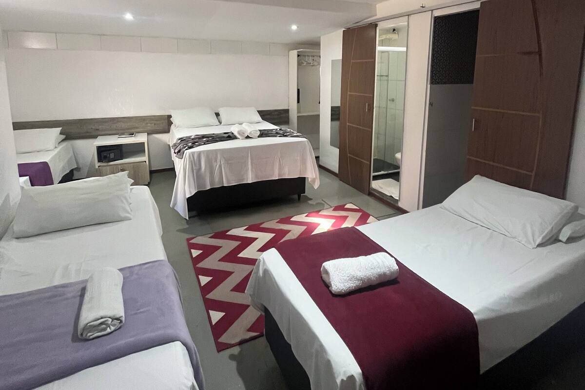 A hotel room with three beds, a red and white patterned rug, and a sliding door closet.