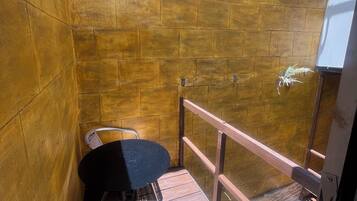 A small outdoor seating area with a wicker chair and a table, a wooden wall, and a metal railing.