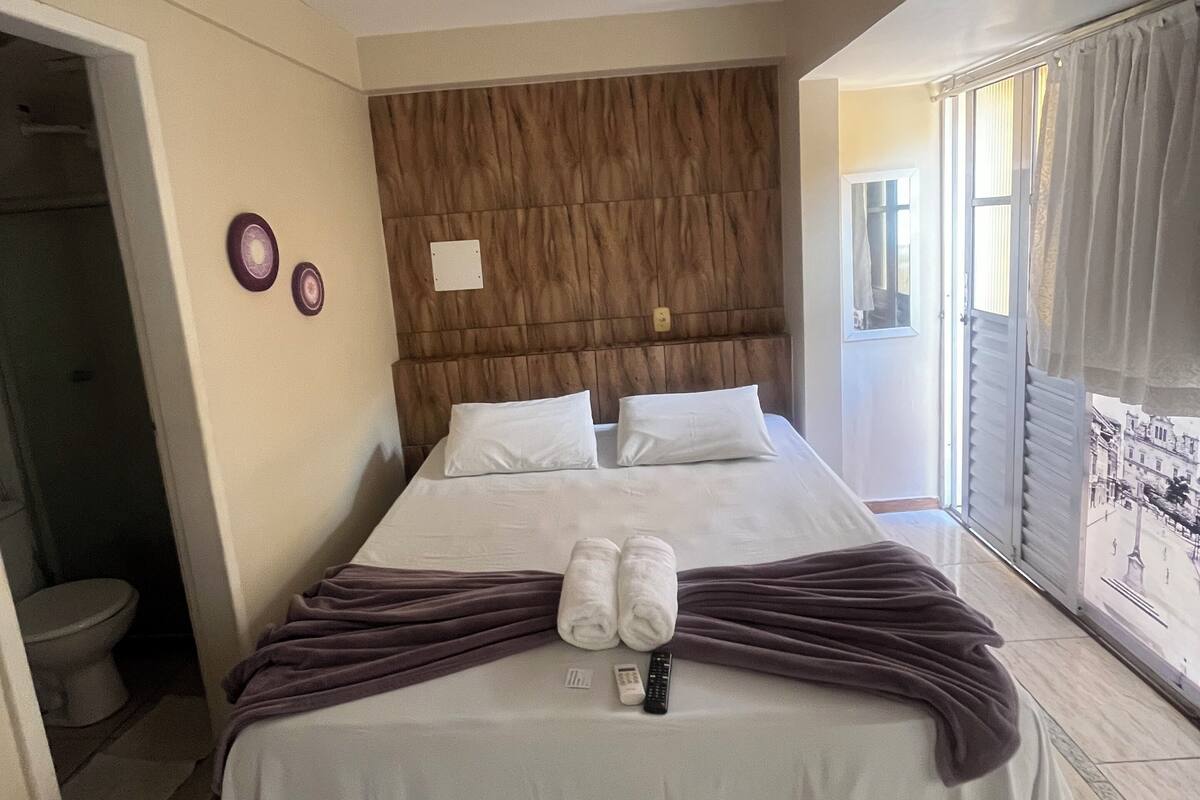 A hotel room with a bed, a bathroom, and a view of the street.