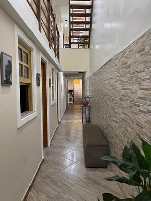 A narrow hallway with a bench, tiled flooring, and a wall with a stone-like pattern. - Pousada Bahia Morena (Salvador)