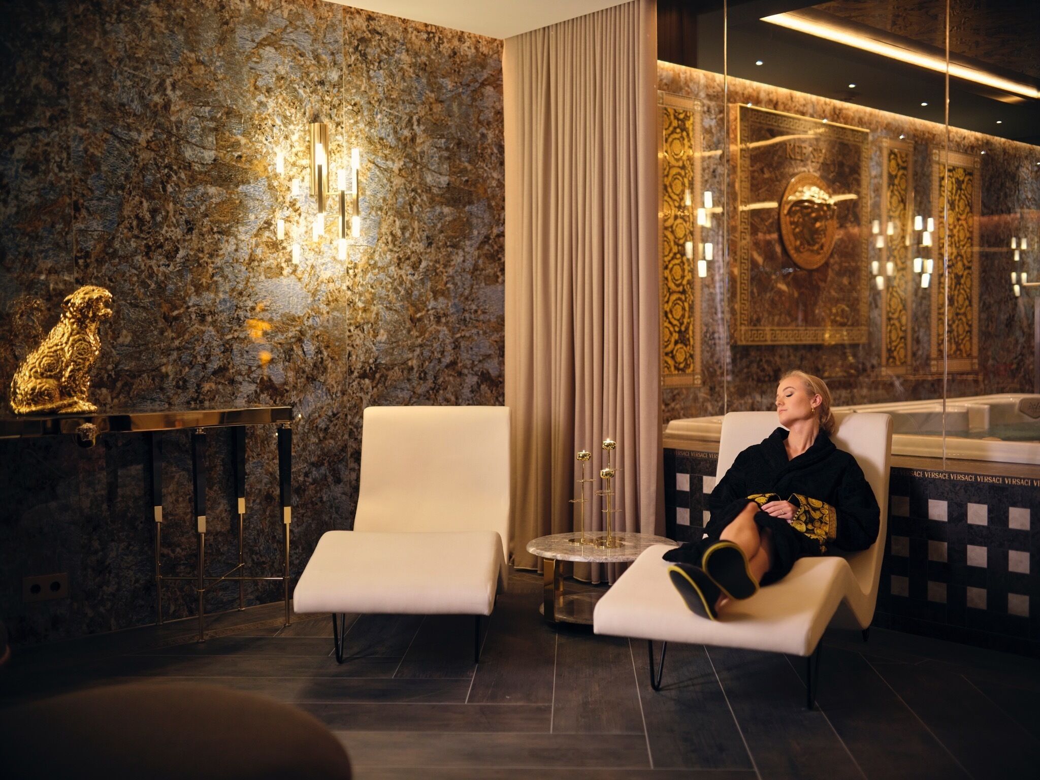 Un hall d’hôtel luxueux avec des murs en marbre, une statue dorée et un espace détente équipé d’un fauteuil de massage.