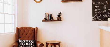 A cozy room with a brown leather armchair, a small round table, and two shelves with books and decorative items.