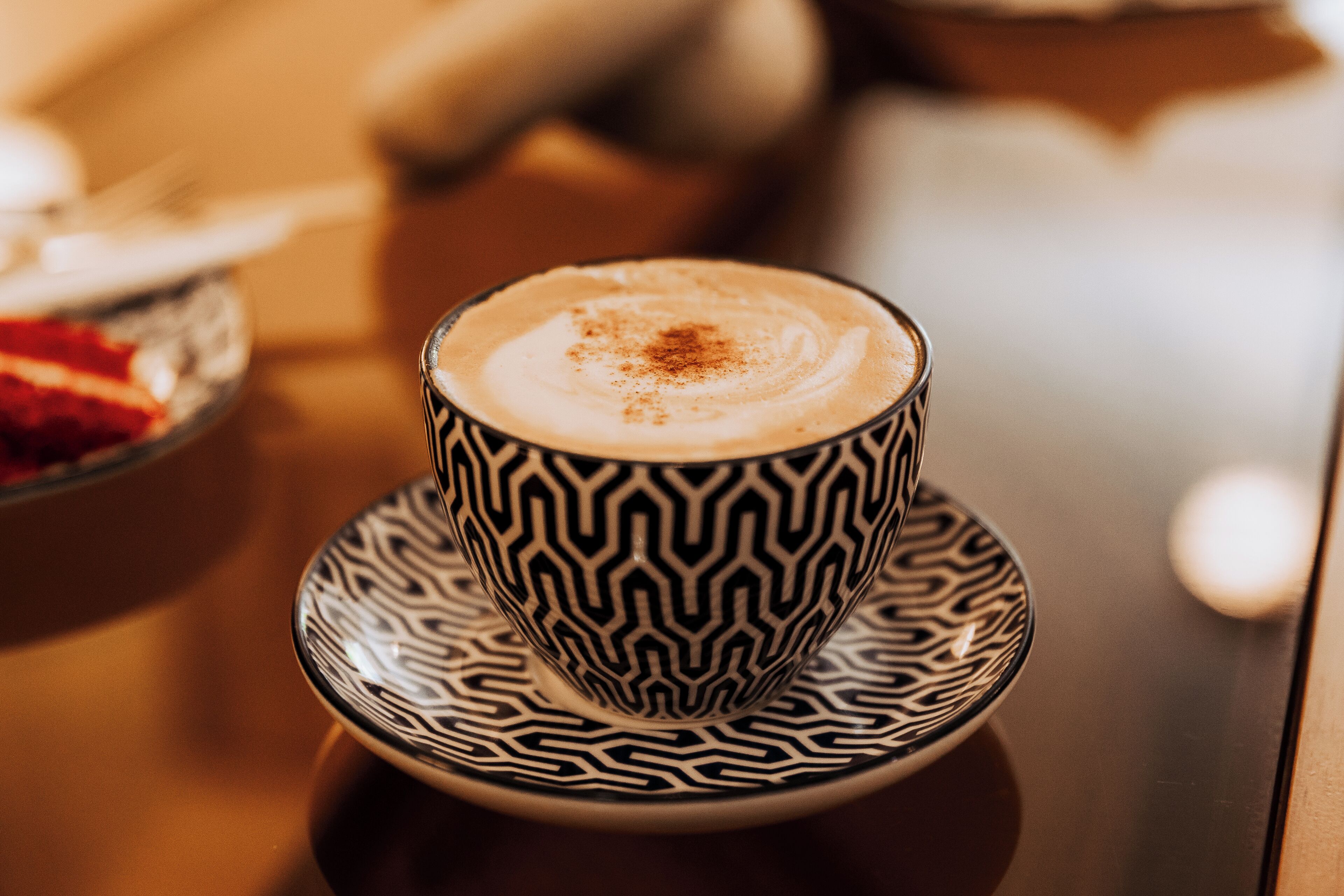 A cup of coffee with a patterned saucer on a table.
