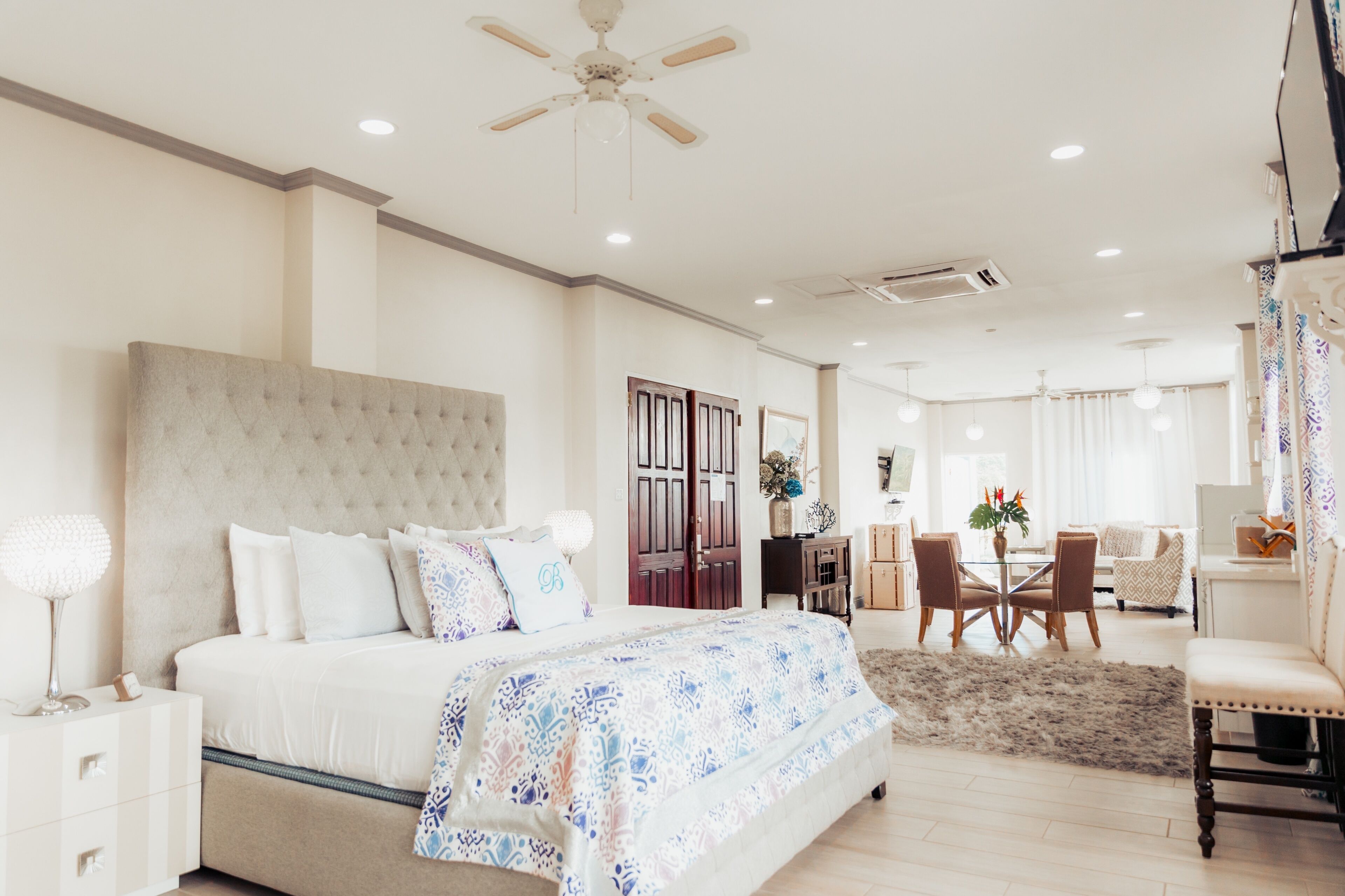 A modern bedroom with a large bed, a ceiling fan, and a dining area with chairs and a table.