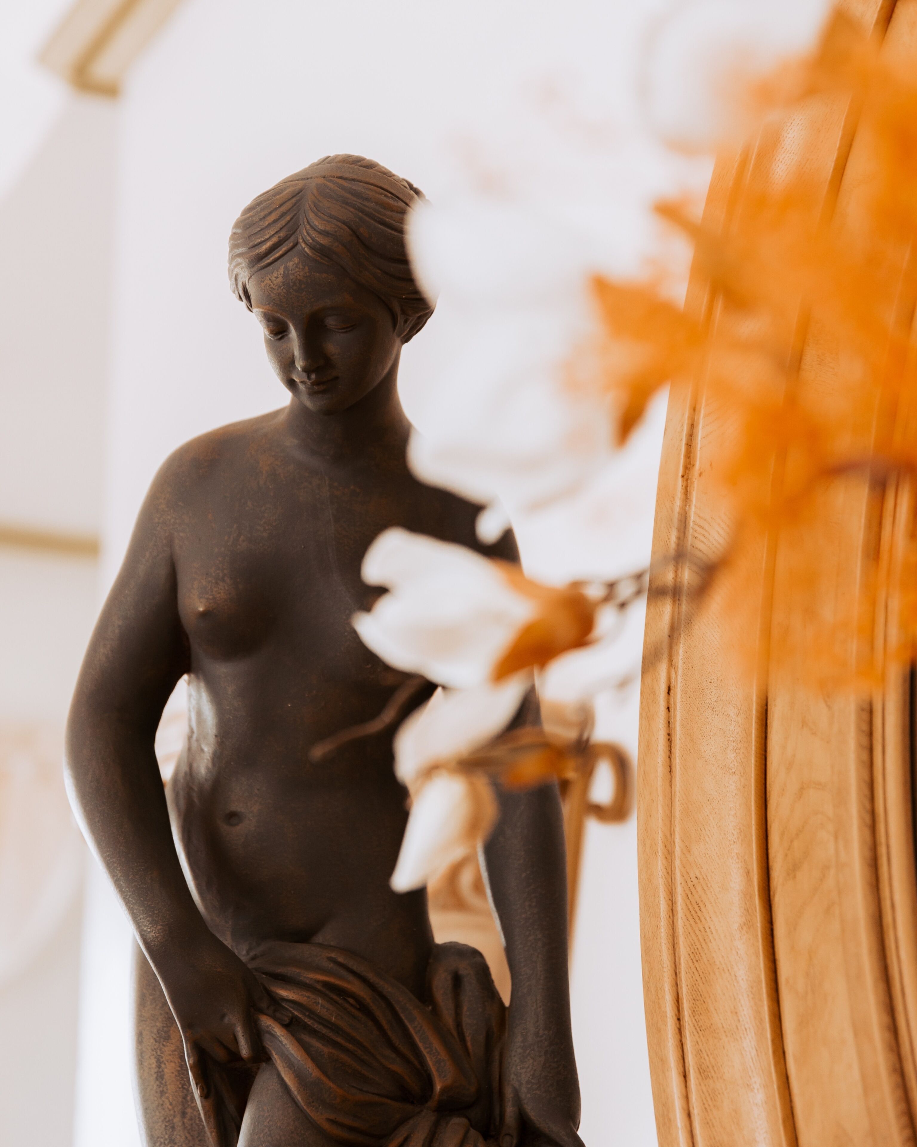 Eine Statue einer Frau in einem Raum mit Holzkonstruktion und weißen Blumen.