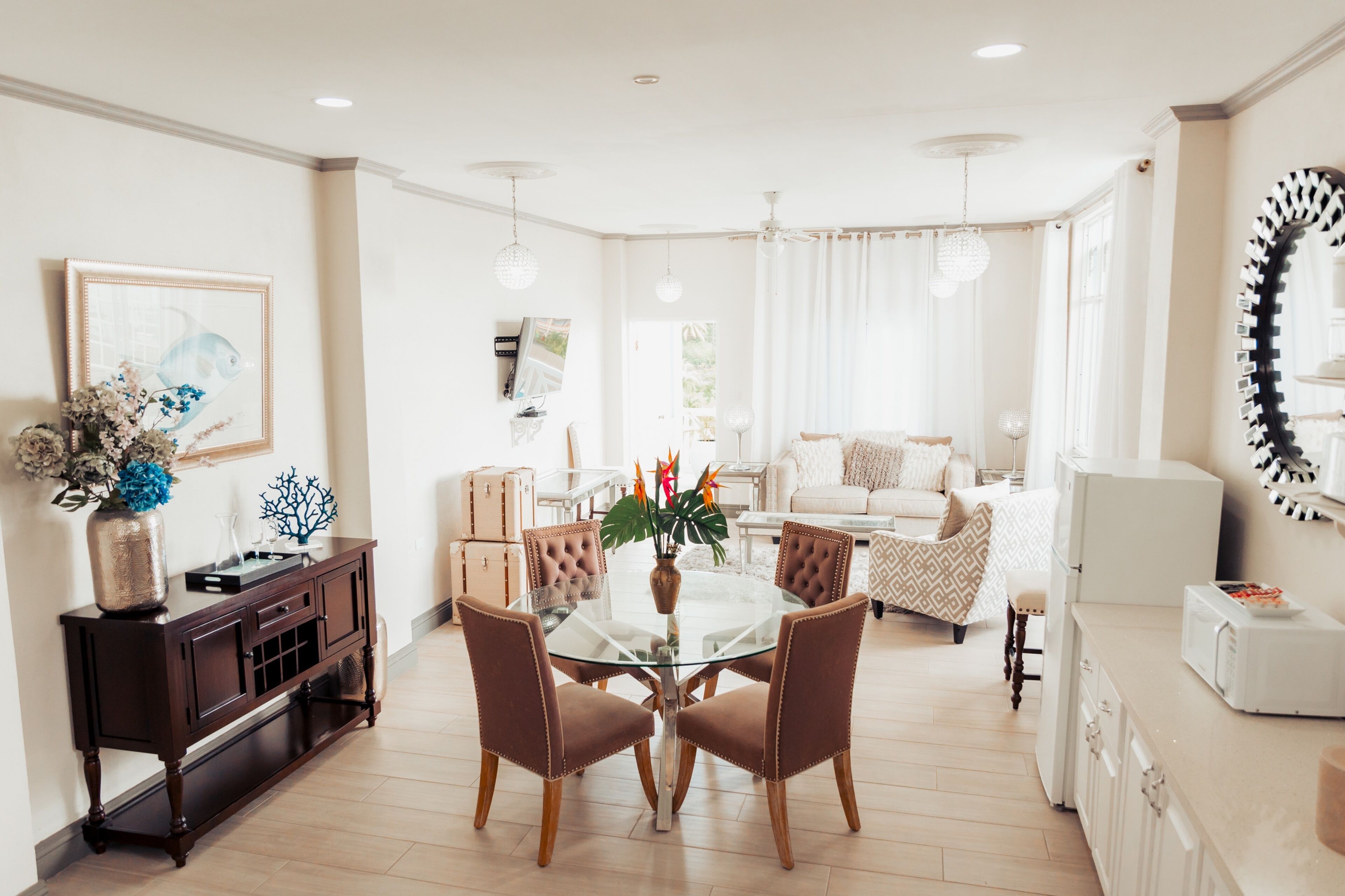 A modern living room with a glass dining table, brown upholstered chairs, a dark wooden console table, and a white sofa.