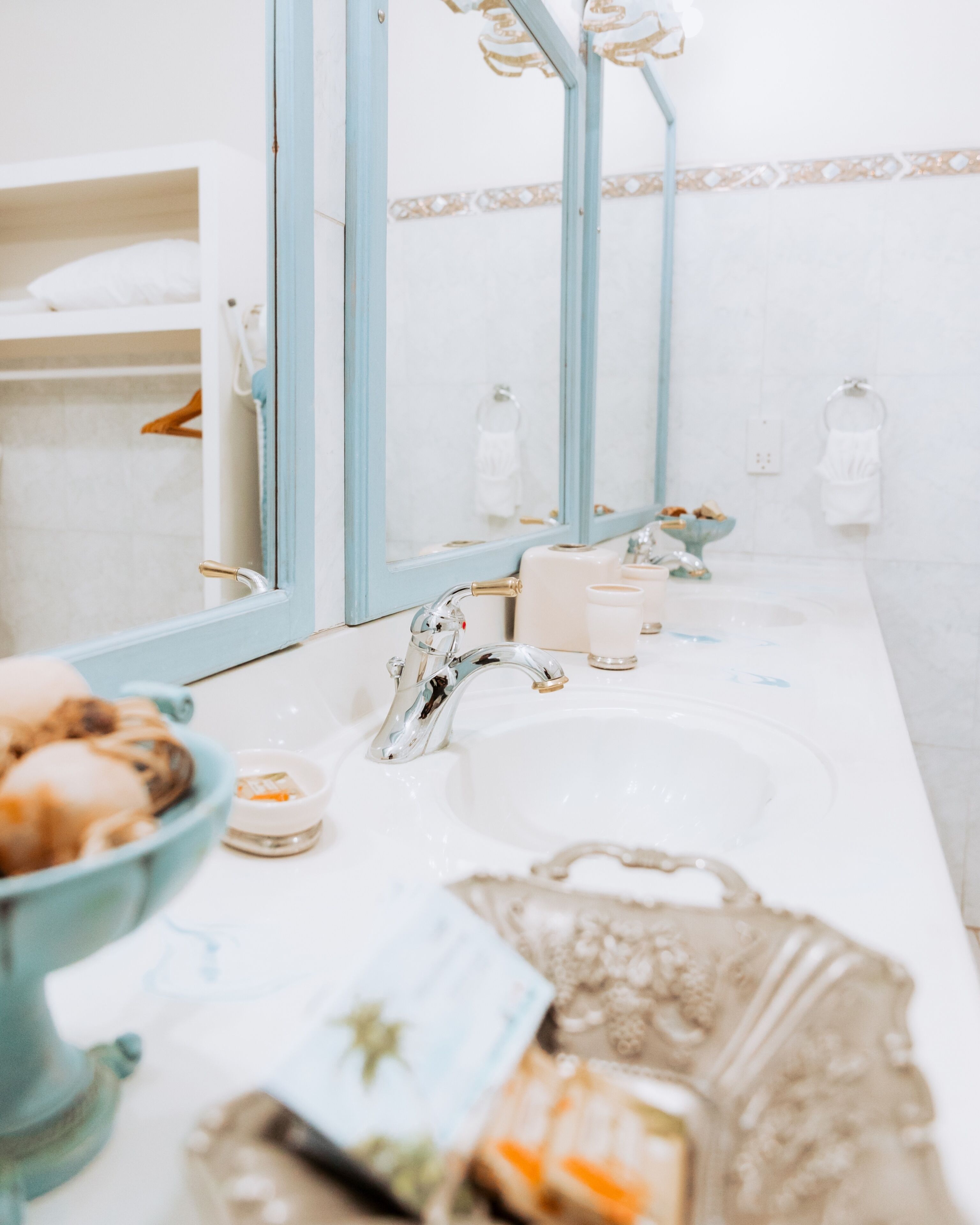 A bathroom with a white sink, a mirror, and a blue-framed mirror. There are toiletries on the sink and a towel rack in the background.