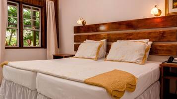 A hotel room with a large bed, wooden headboard, two bedside lamps, a nightstand with a phone, and a window with curtains.