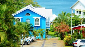 A blue building with a white roof, surrounded by lush greenery and parked cars. - Beachcombers Hotel (Villa)