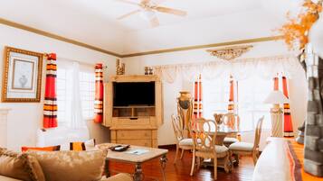 A living room with a fireplace, a television, a dining table with chairs, and a ceiling fan.