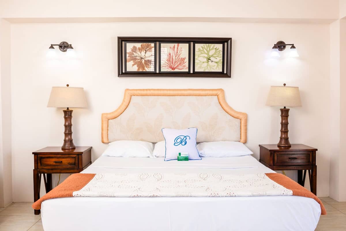 A neatly made bed with a decorative headboard, two bedside tables with lamps, and framed artwork above the bed.