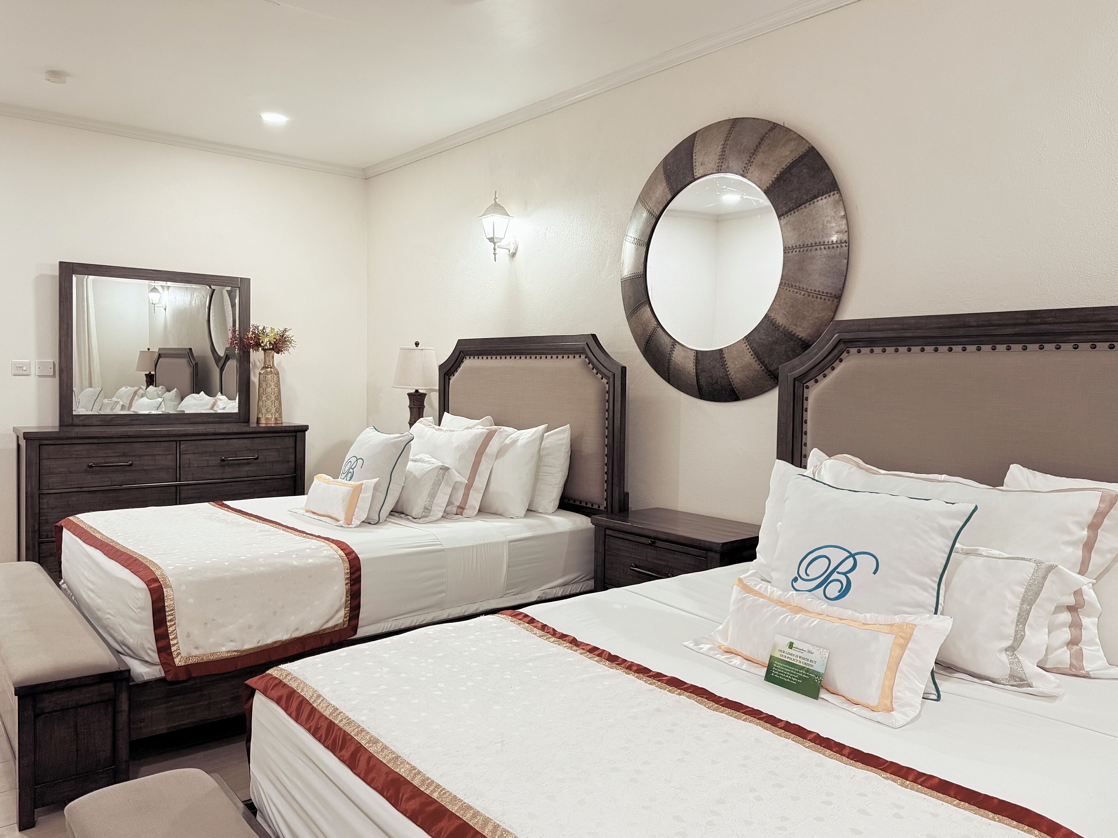A hotel room with two beds, a large mirror, and a wall-mounted lamp.