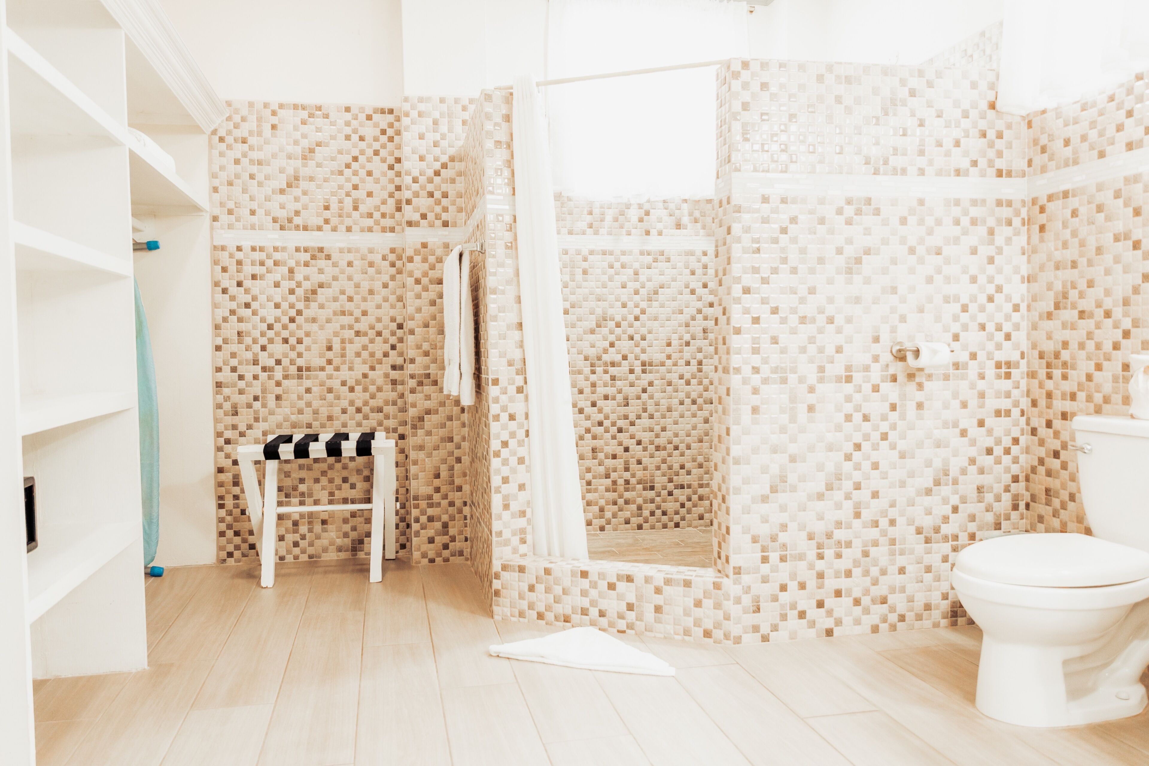 A bathroom with a mosaic tile shower, a white toilet, and a bench with towels.