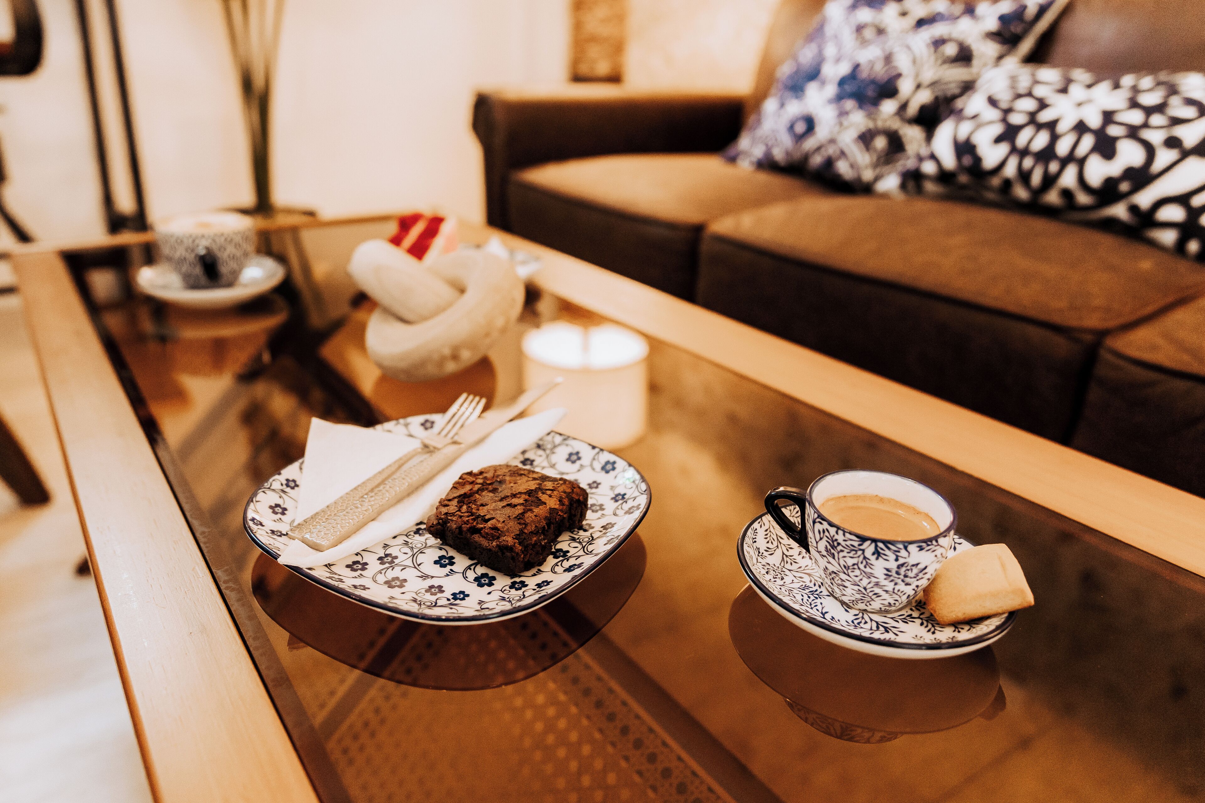 A cozy living area with a glass coffee table, a plate with a piece of cake, a cup of coffee, and a candle.