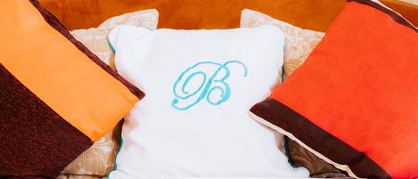 A bed with a white pillow featuring a monogram, surrounded by pillows in various colors.