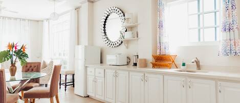 A bright kitchen with white cabinets, a round mirror, and a dining area with a glass table and chairs.