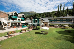 Relax in the hotel's serene outdoor space, featuring a central building with a green roof, benches, and picnic tables.
