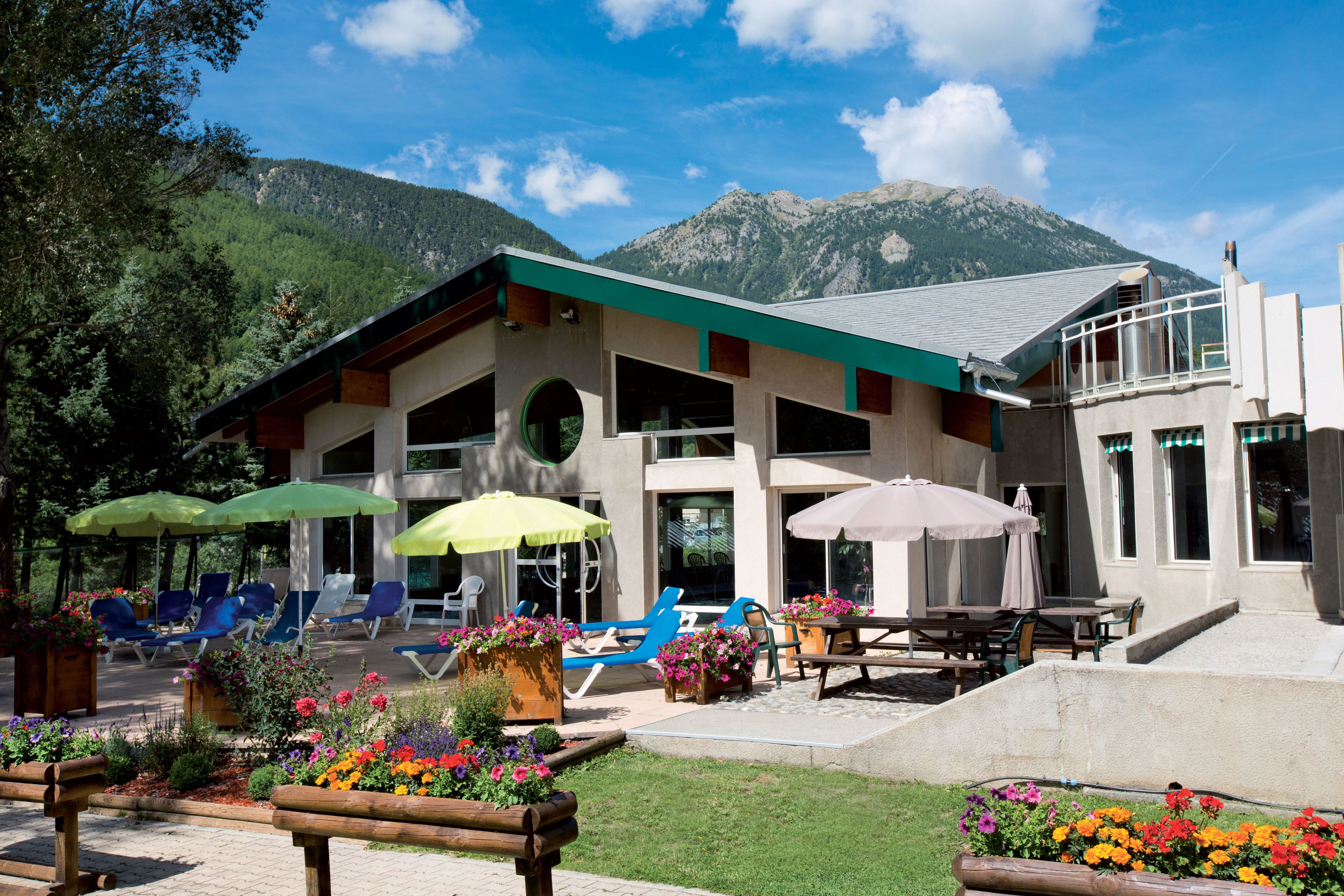 A hotel with outdoor seating, flower beds, and mountain views.